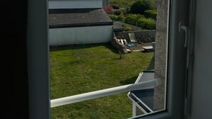 A view from a window of a house with a sloped roof, a lawn, and a stone wall. - Maison à 100m de la Plage (Treffiagat)