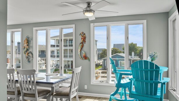 A dining area with a table and chairs, large windows, and a view of neighboring houses. - Waterfront 5BR • Dock • BYO Boat • Sleeps 16 • 2 Living Rooms • 2 Miles to Beach (Selbyville)