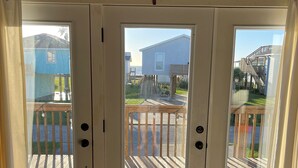 A set of glass doors leading to a wooden deck with a view of a residential area. - Oceanview Beach House - steps from the beach, really close to Galveston. TipSea! (Galveston)