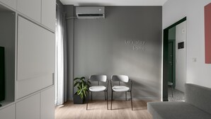 Una sala de estar moderna con un sofá gris, dos sillas blancas, una planta en maceta y un aire acondicionado de pared.