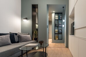 Ett modernt vardagsrum med en soffa, ett soffbord i glas, en krukväxt och en bokhylla.