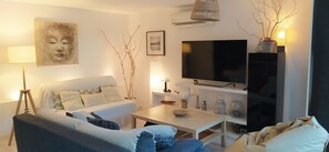 Uma sala de estar moderna com um sofá, mesa de centro e televisão. Há um abajur, galhos decorativos e uma moldura na parede.