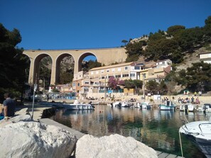 Uma vila costeira com uma ponte de pedra imponente, barcos atracados na orla marítima e edifícios residenciais com varandas.