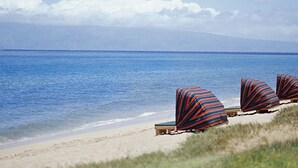 En strand med liggestole og parasoller, en klar himmel og et roligt hav.