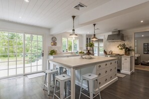 A spacious kitchen with a large island, pendant lighting, and a view of the outdoors through large windows.