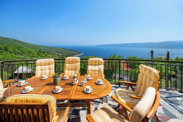 A wooden table with chairs and teapots, overlooking a scenic view of a body of water and hills. - Pretty villa with above ground pool, magnificent sea views (Plomin - Zagorje)