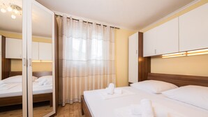 Une chambre d’hôtel avec un plancher en bois, un lit avec du linge de maison blanc, un meuble avec miroir et un rideau à rayures.