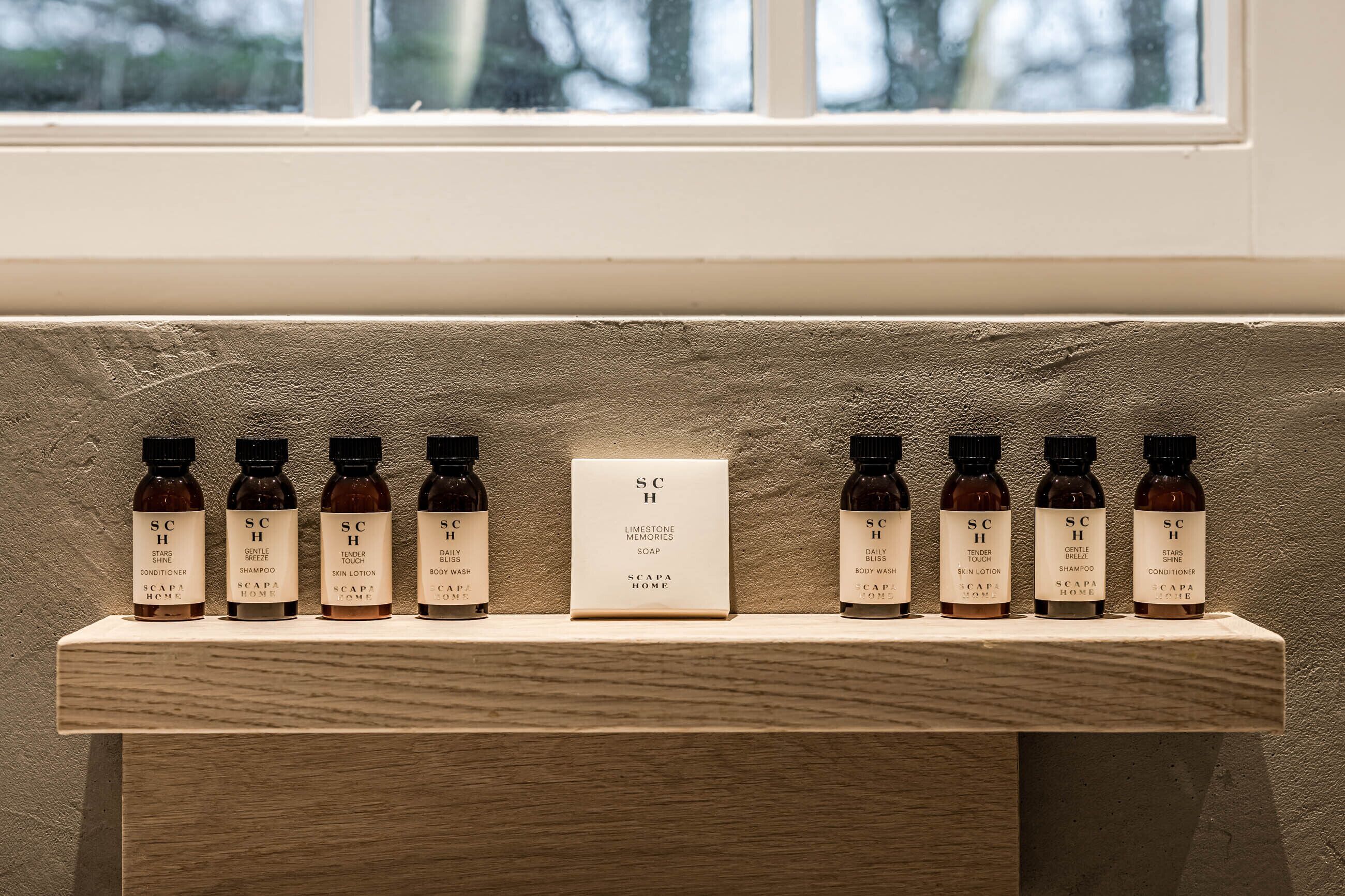 Een houten plank met diverse huidverzorgingsproducten en een bordje met de tekst 'SC H Limestone Memories Soap'.