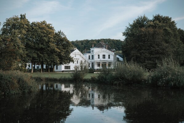 A large white building with a symmetrical facade, a central tower, and a reflection in the water in front. - Landgoed Altenbroek (Voeren)