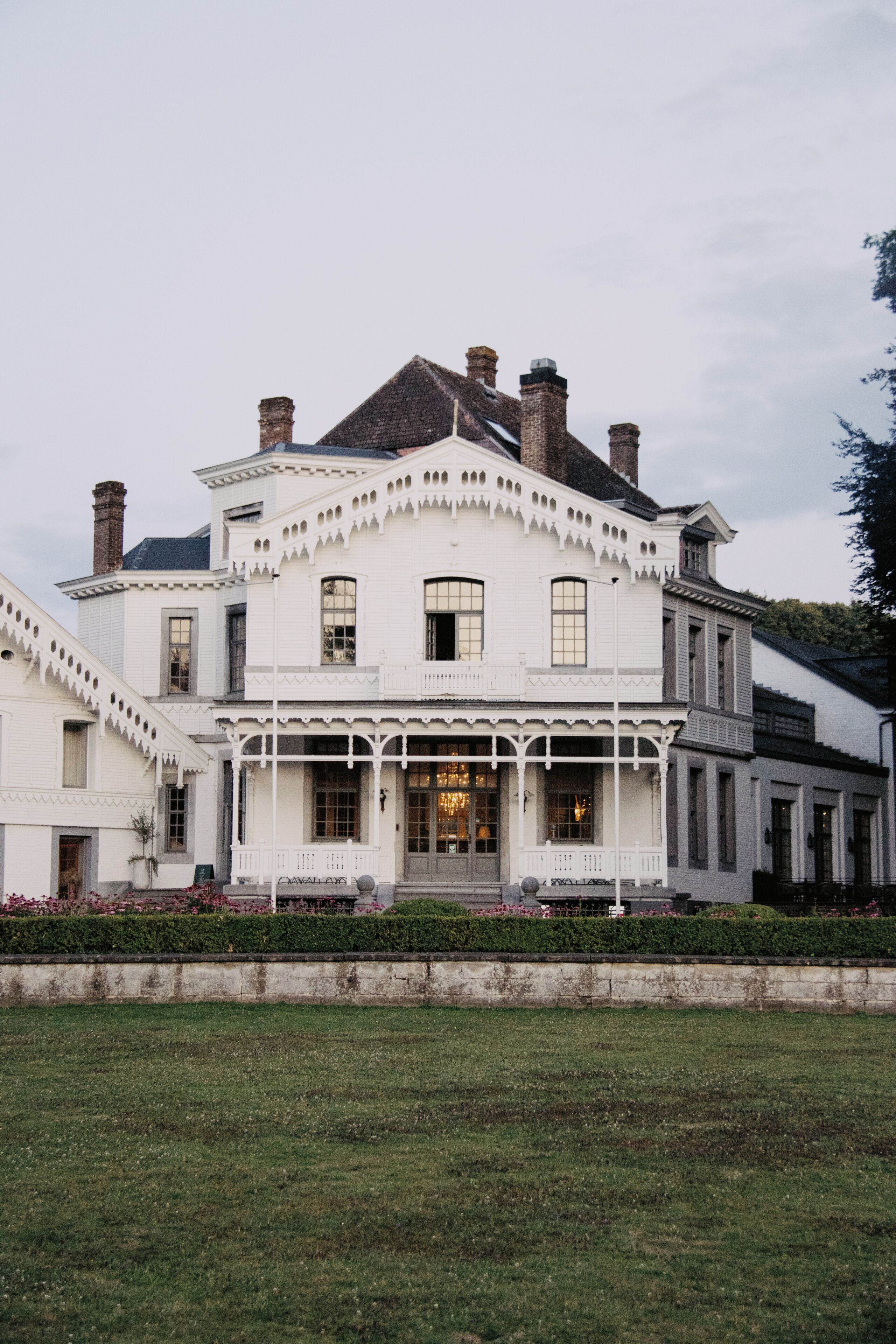 Un grand bâtiment blanc à deux étages, doté d’une façade symétrique, de nombreuses cheminées et d’une entrée centrale avec un porche.