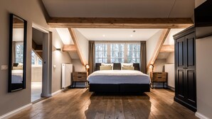 A bedroom with a large bed, wooden beams, a window with curtains, and a view of trees. - Landgoed Altenbroek (Voeren)