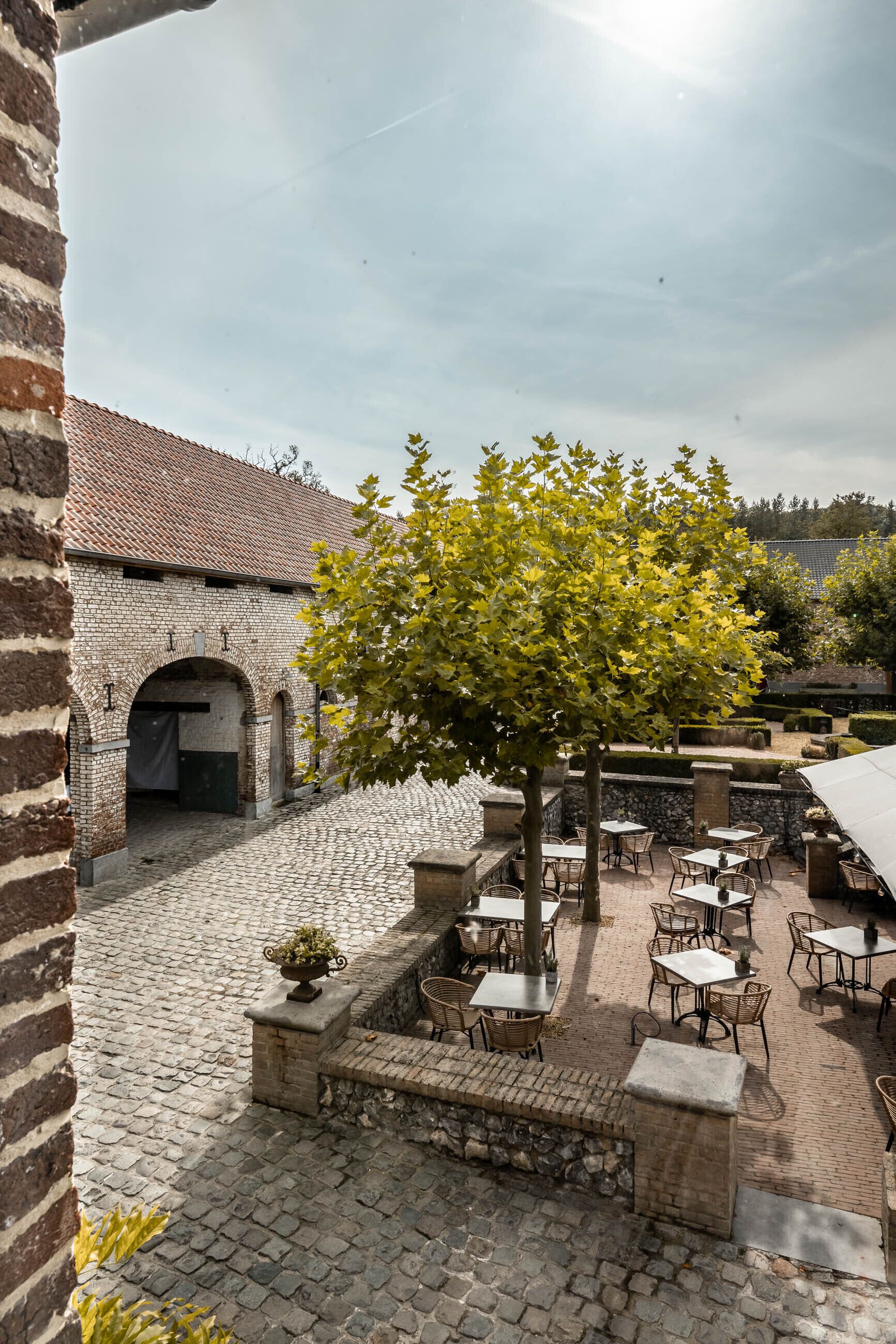 Une cour extérieure avec un sol pavé de pierres, des bancs en pierre et des tables avec des chaises.