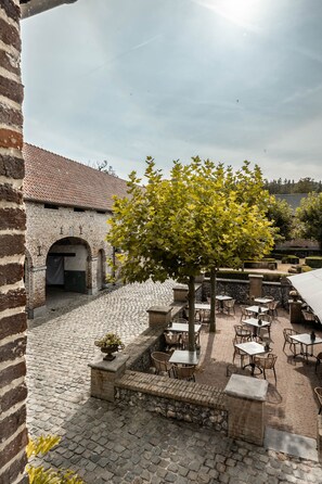 An outdoor courtyard with cobblestone flooring, stone benches, and tables with chairs. - Landgoed Altenbroek (Voeren)