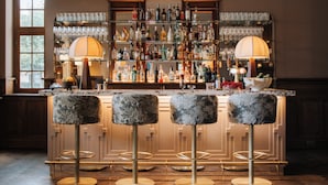 A bar area with a bar counter, stools, and a variety of bottles and glasses. - Landgoed Altenbroek (Voeren)