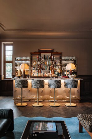 A bar area with a bar counter, stools, and a variety of bottles and glasses. - Landgoed Altenbroek (Voeren)