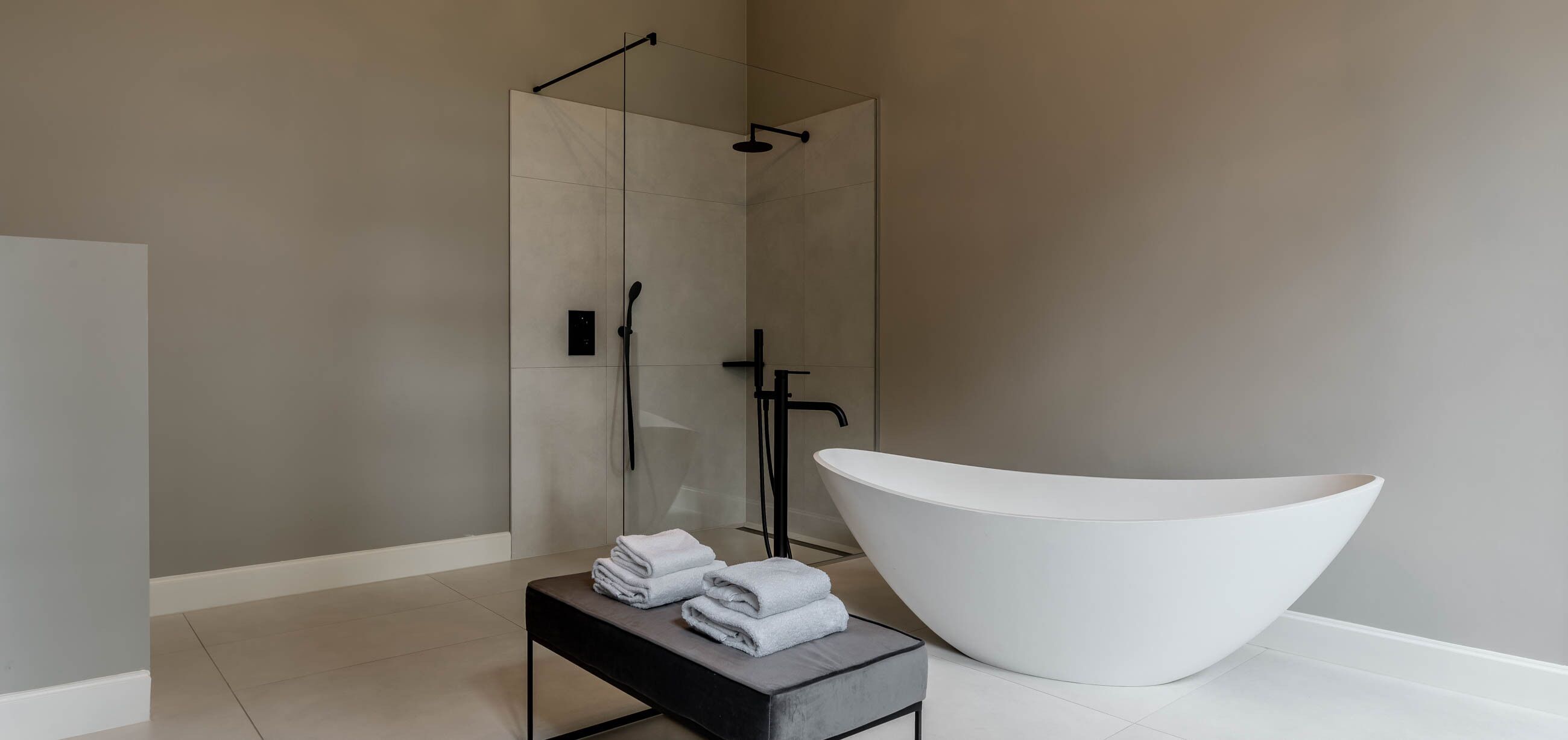 Un baño moderno con una bañera blanca grande, una ducha con cerramiento de vidrio y toallas ordenadas sobre una mesita.