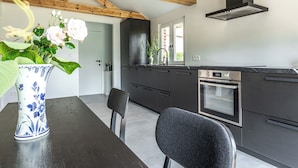 A modern kitchen with dark cabinetry, a built-in oven, and a window with a view. - Landgoed Altenbroek (Voeren)