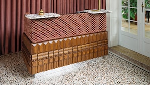 A room with a checkered bench, a wall-mounted light fixture, and a door leading to an outdoor area. - Landgoed Altenbroek (Voeren)