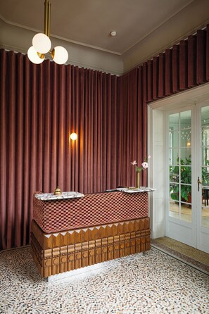 A room with a checkered bench, a wall-mounted light fixture, and a door leading to an outdoor area. - Landgoed Altenbroek (Voeren)