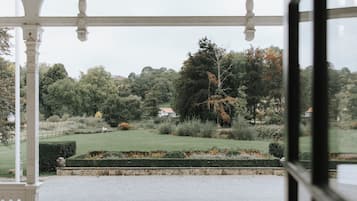 Een overdekt buitengebied met uitzicht op een aangelegde tuin en een gebouw in de verte.
