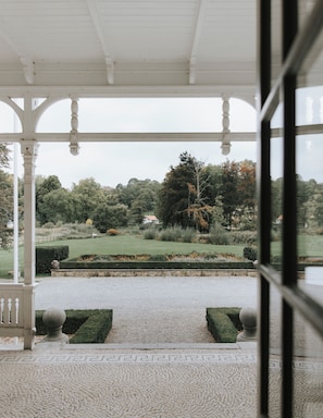 A covered outdoor area with a view of a landscaped garden and a distant building. - Landgoed Altenbroek (Voeren)
