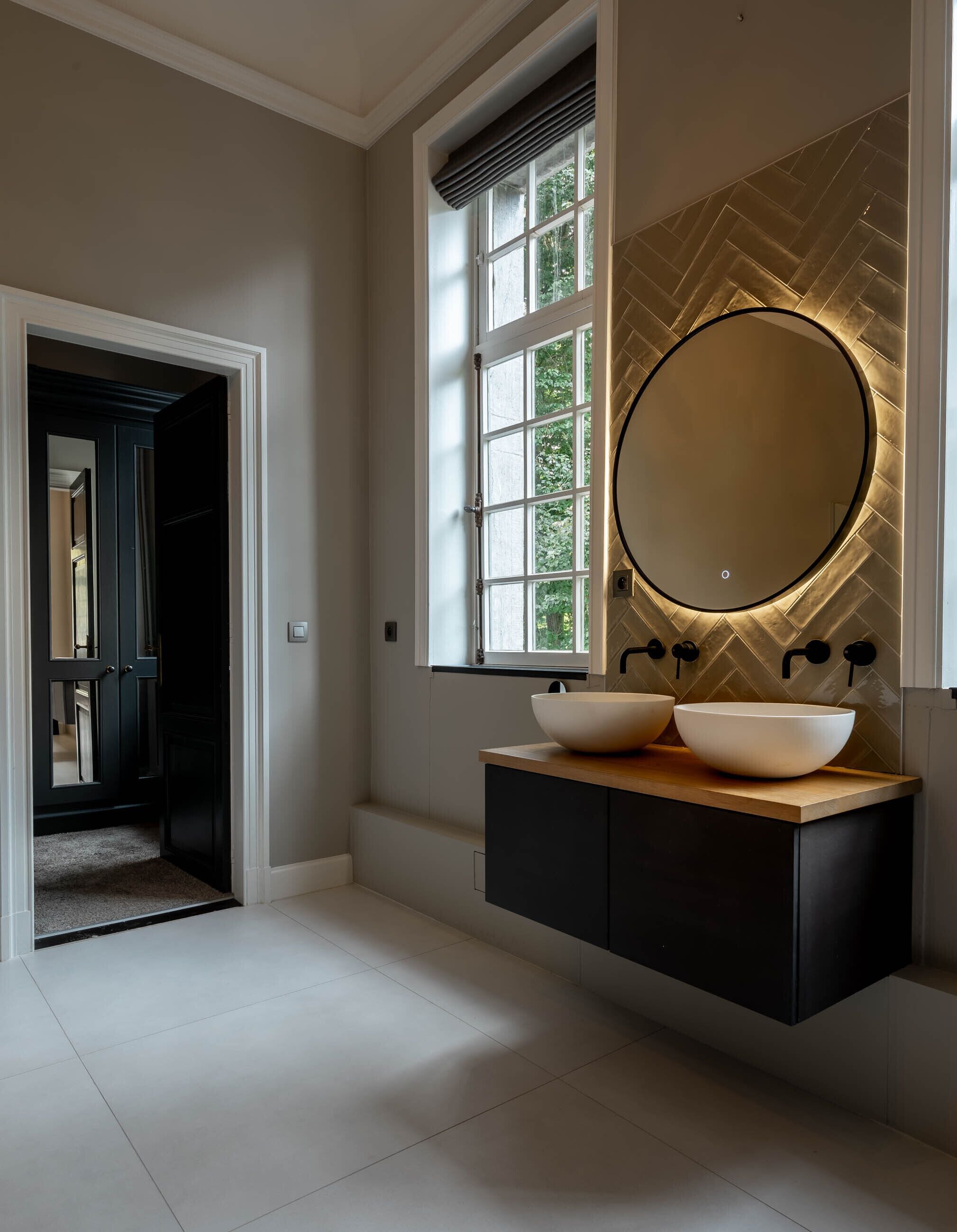 Een moderne badkamer met een grote spiegel, twee wasbakken en een backsplash met een herringbone patroon.