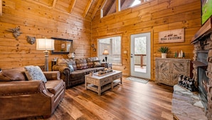Ein Interieur einer Blockhütte mit Holzboden, Ledersofas, einem Couchtisch, einem Kamin und einem Schild mit der Aufschrift 'Bear Crossing'.
