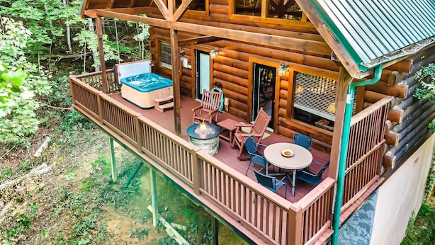 Eine Holzhütte mit Whirlpool, Sitzgelegenheiten im Freien und einer Terrasse mit Blick auf einen Wald.