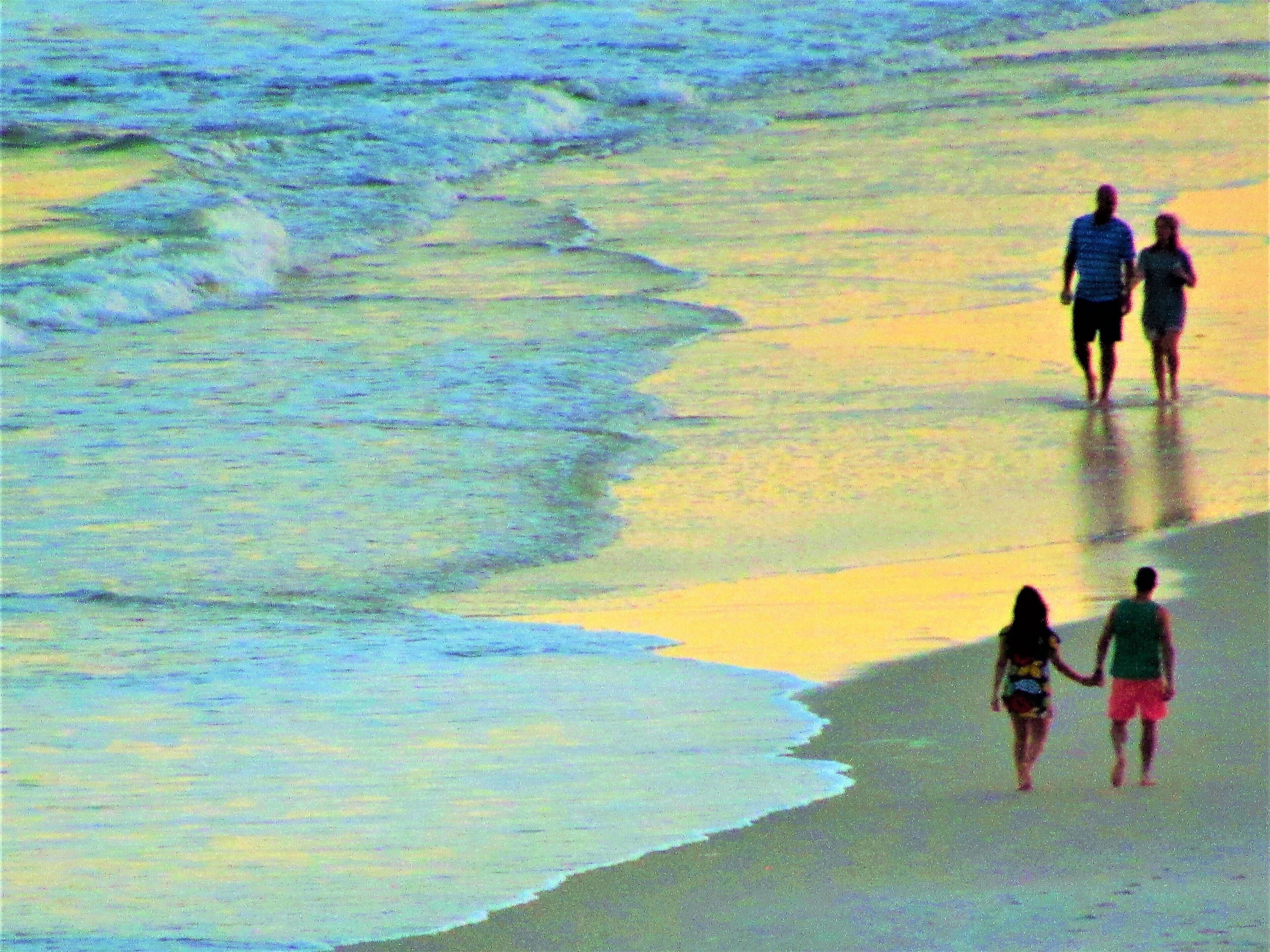 A beach scene with people walking along the shore.