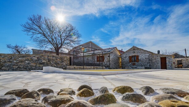 A stone building with a metal roof structure, a stone wall, and a paved area with rocks. - Ranch Wild North (Benkovac)