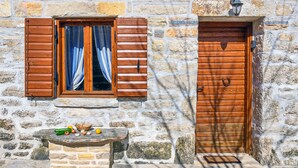 A stone building with a wooden door and window with shutters, a stone bench with vegetables, and a small table. - Ranch Wild North (Benkovac)
