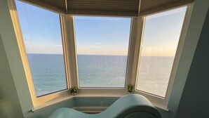 Una stanza con un divano curvo di un azzurro chiaro rivolto a una finestra a bovindo con vista sul mare.