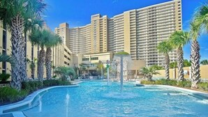 Un hotel con una grande piscina, palme e un grattacielo sullo sfondo.