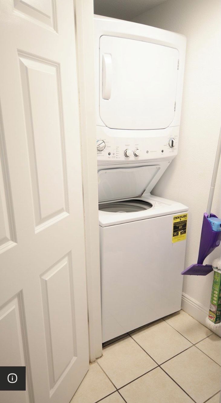 A laundry room with a front-loading washer and dryer, a door, and a purple cleaning tool on a shelf.