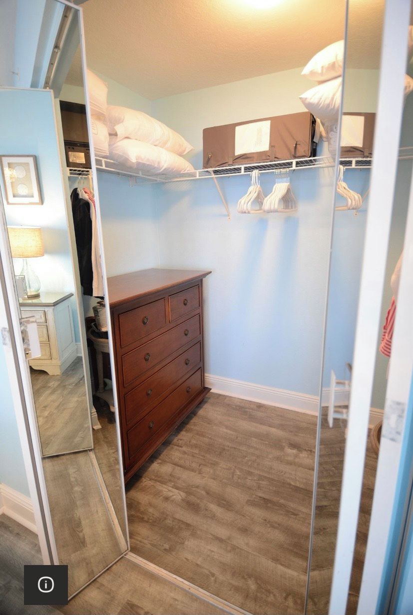 A bedroom with a wooden dresser, a bed with white bedding, and a closet with hanging clothes.