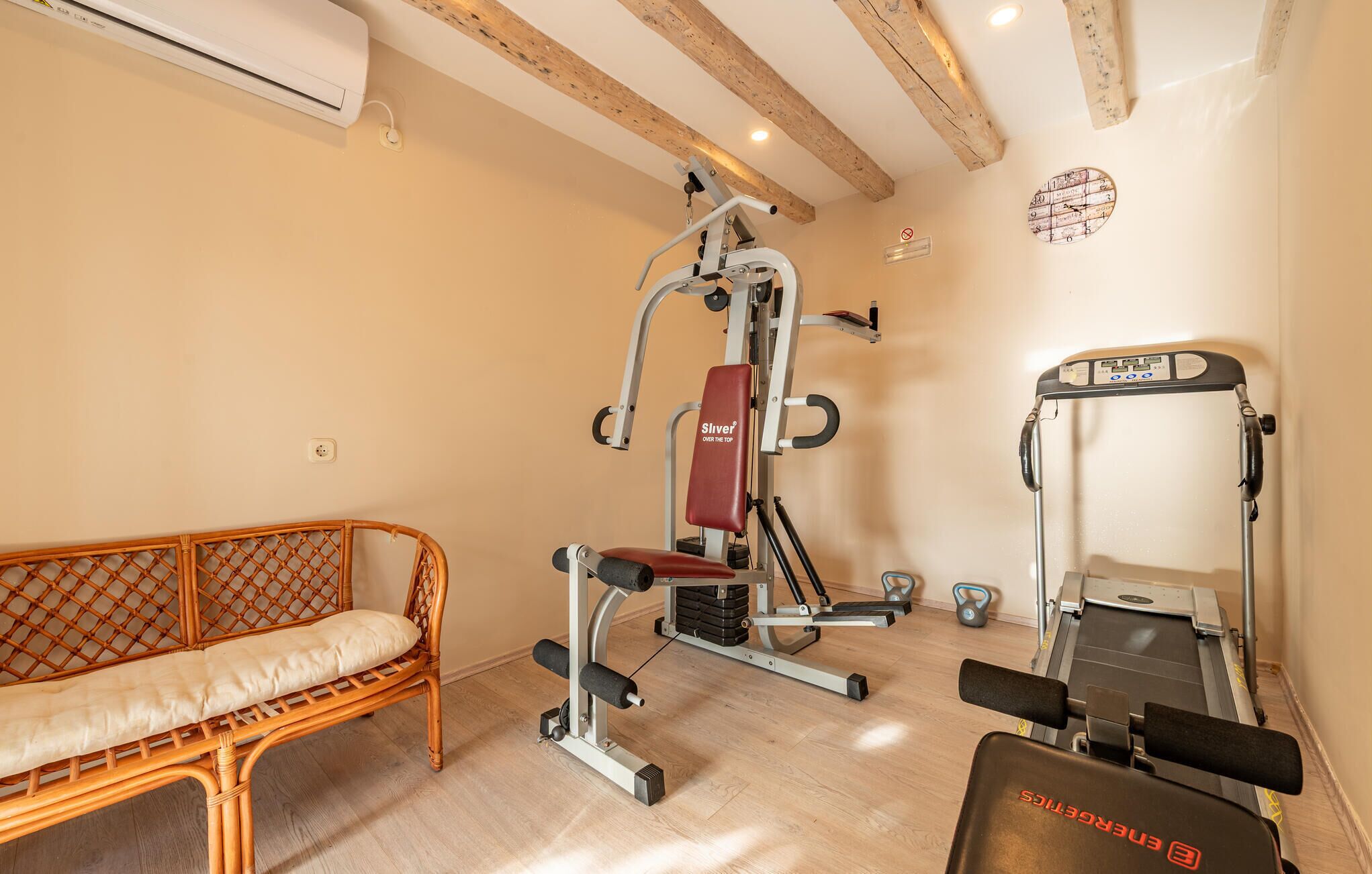 Une salle de sport à domicile équipée d’un banc de musculation, d’une machine à câbles et d’un tapis de course.