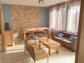Una sala de estar con una mesa de comedor de madera, sillas de mimbre, un sofá con cojines y una pared de piedra.