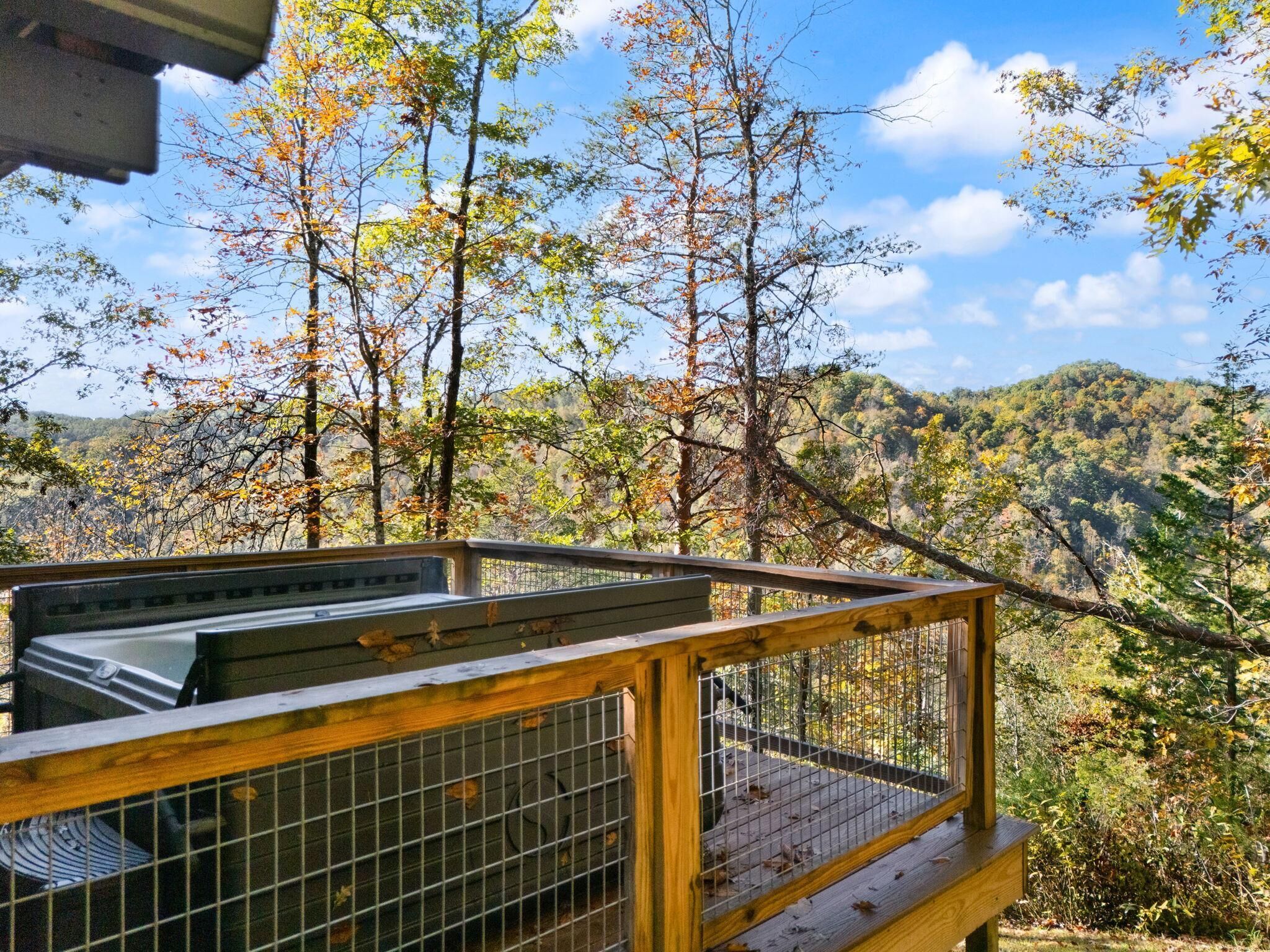 Une terrasse en bois avec une rambarde en métal, donnant sur une colline boisée.