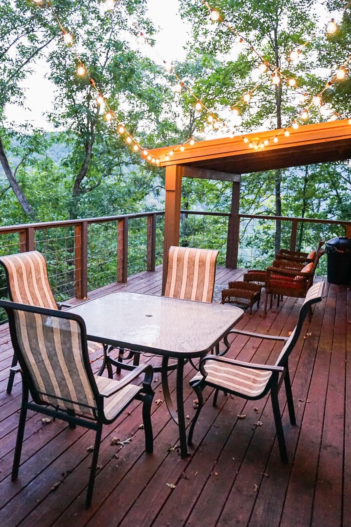 A wooden deck with a table and chairs, surrounded by trees and string lights.