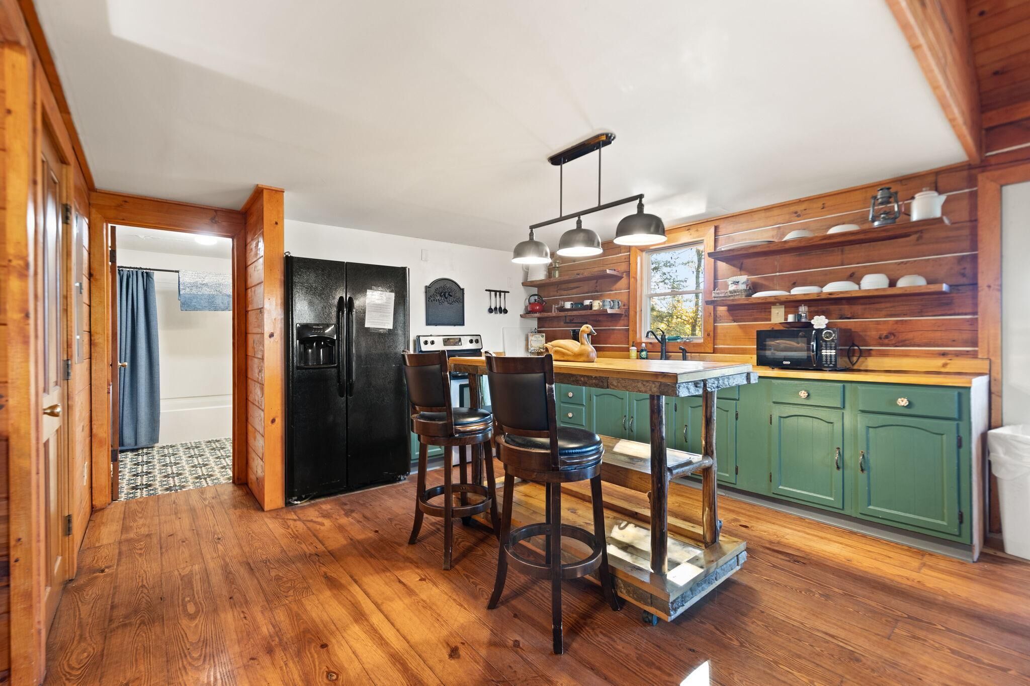 A kitchen with wooden cabinets, a black refrigerator, and a wooden island with bar stools.