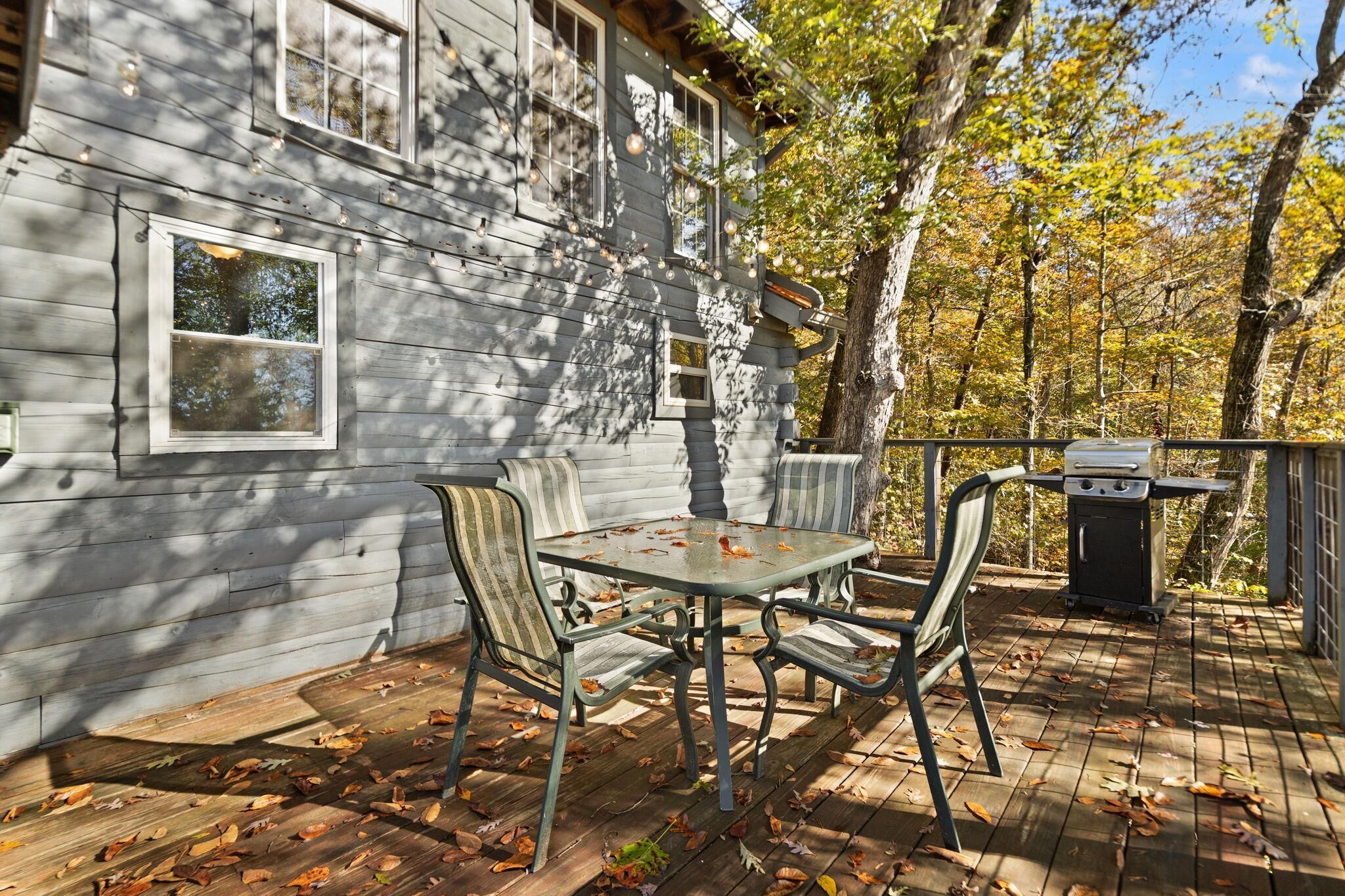 A wooden deck with a table and chairs, a barbecue grill, and a house with windows.