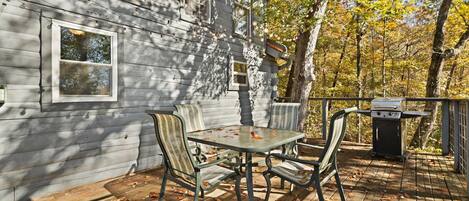 A wooden deck with a table and chairs, a barbecue grill, and a house with windows.