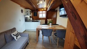Acogedor espacio tipo loft con comedor, kitchenette y un sofá gris con un cojín decorativo.