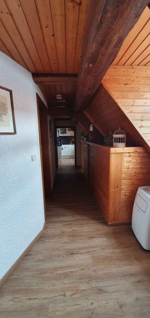 A narrow hallway with wooden floors and walls, leading to a kitchen area with wooden cabinets and a white appliance.