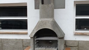 Un horno de pizza de piedra al aire libre con chimenea, frente a una pared blanca con ventanas.