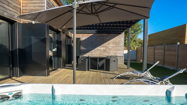 A swimming pool with a wooden deck, lounge chairs, and a covered patio area. - Modern house with great facilities and a large jacuzzi (Crozon)