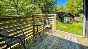 Une terrasse en bois avec une table et deux chaises, donnant sur une zone herbeuse où se trouve une petite construction en bois.