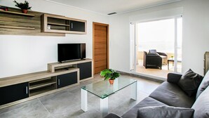 Ein modernes Wohnzimmer mit Flachbildfernseher, Einbauschränken, einem Glastisch und einer Couch.