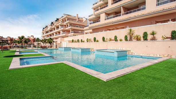 Ein Resort mit mehreren Schwimmbecken, einem gepflegten Rasen und einem großen Gebäude mit Balkonen.