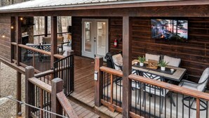 Una cabaña de madera con un porche cubierto, mobiliario exterior y un televisor montado.
